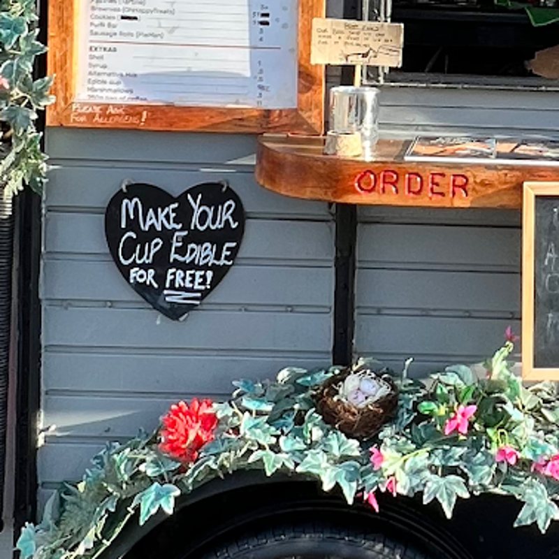 A heart-shaped chalkboard reading Make your cup edible for free, beside the order shelf on the trailer.