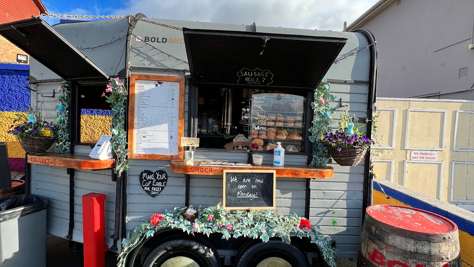 The grey Bold & Brass horsebox trailer with its hatches open, chalkboards, a pastry case and timber order and collect shelves.